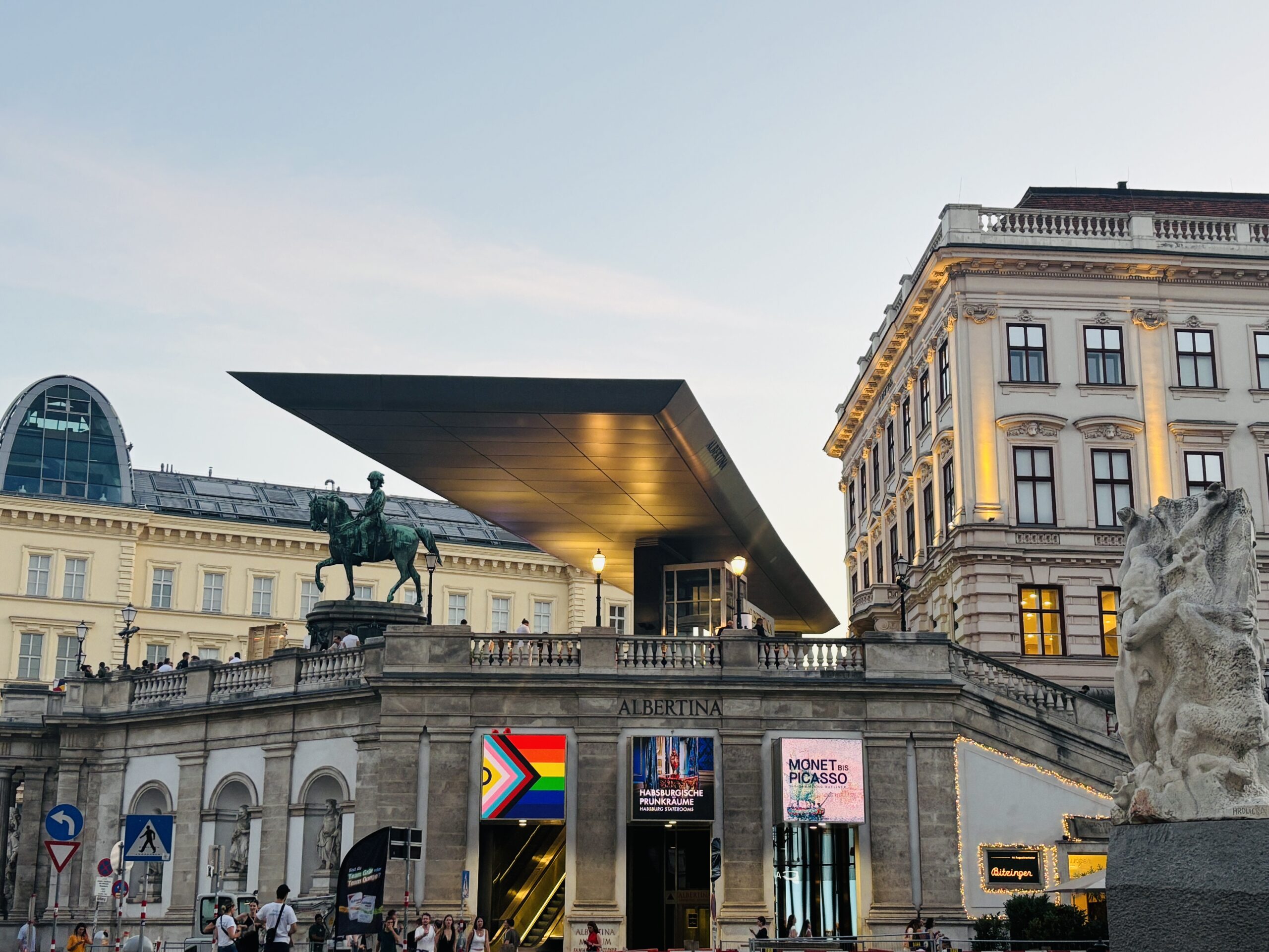 Evening photo of the Albertina Museum in Vienna with modern roof, equestrian statue, and illuminated signage