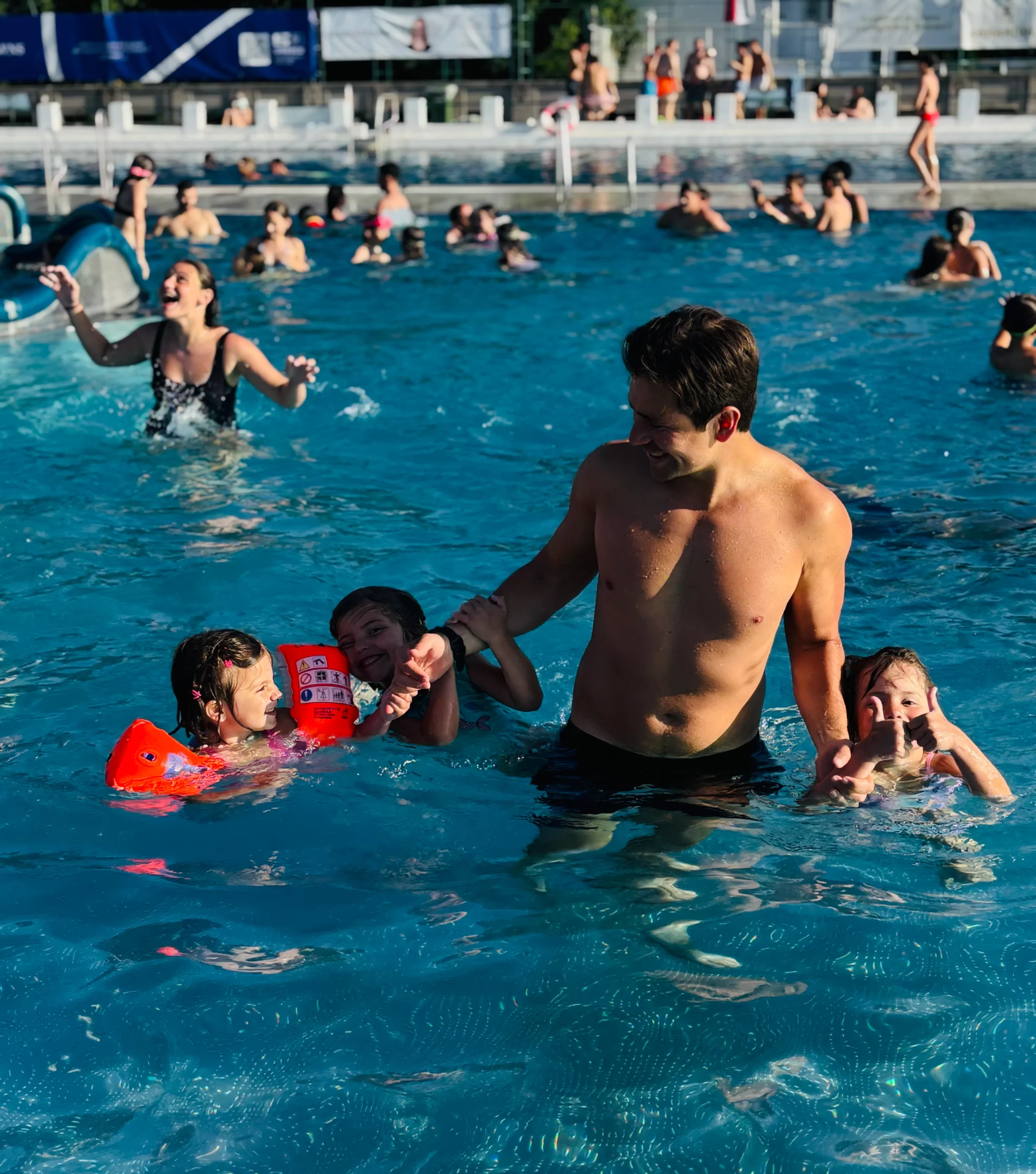 A father swimming with his children in the outdoor thermal pool at Thermalstrandbad Baden, Austria, surrounded by lush greenery and sunlit waters.