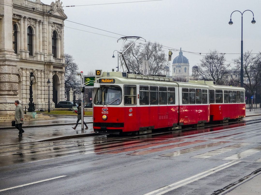 Red tram traveling along a wet city street in Vienna, Austria